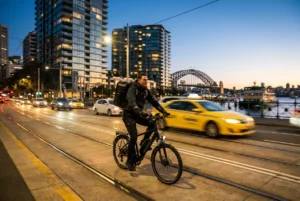 Courier biking through a busy Sydney street at dusk